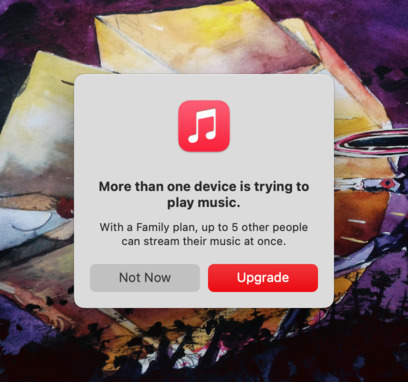 Visible over a desktop wallpaper is a native macOS dialog popup. At the top of the popup is the Apple Music logo. The text reads &ldquo;More than one device is trying to play music. With a Family plan, up to 5 other people can stream their music at once.&rdquo; with the ability to select Not Now or Upgrade.
